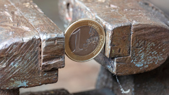 Een euromunt die tussen metalen blokken wordt samengeperst, als symbool voor inflatie