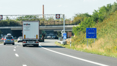 Vrachtwagen rijdt langs het bord “Nederland” bij de grens tussen Duitsland en Nederland